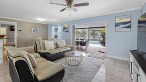 A living room with a sofa, armchair, coffee table, ceiling fan, and a TV.