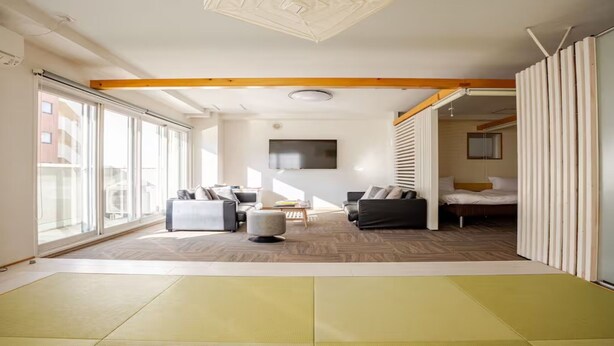 Une chambre d’hôtel moderne dotée d’une grande porte coulissante, d’un canapé, d’un lit et d’un téléviseur fixé au mur.