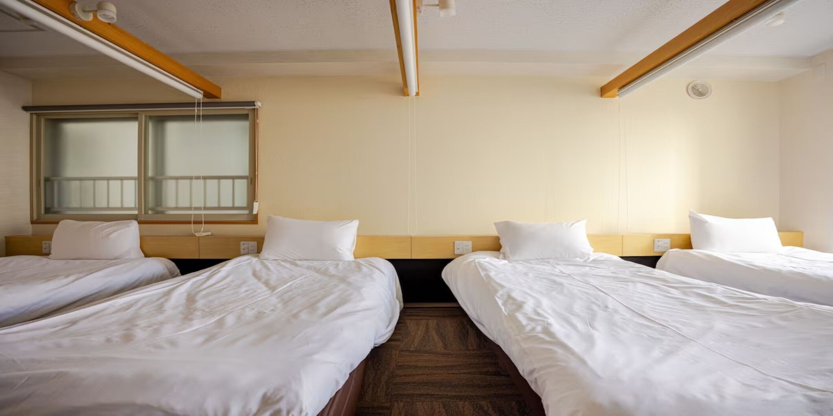 Une chambre d’hôtel avec deux lits simples, une fenêtre avec des stores et un plafond en bois.