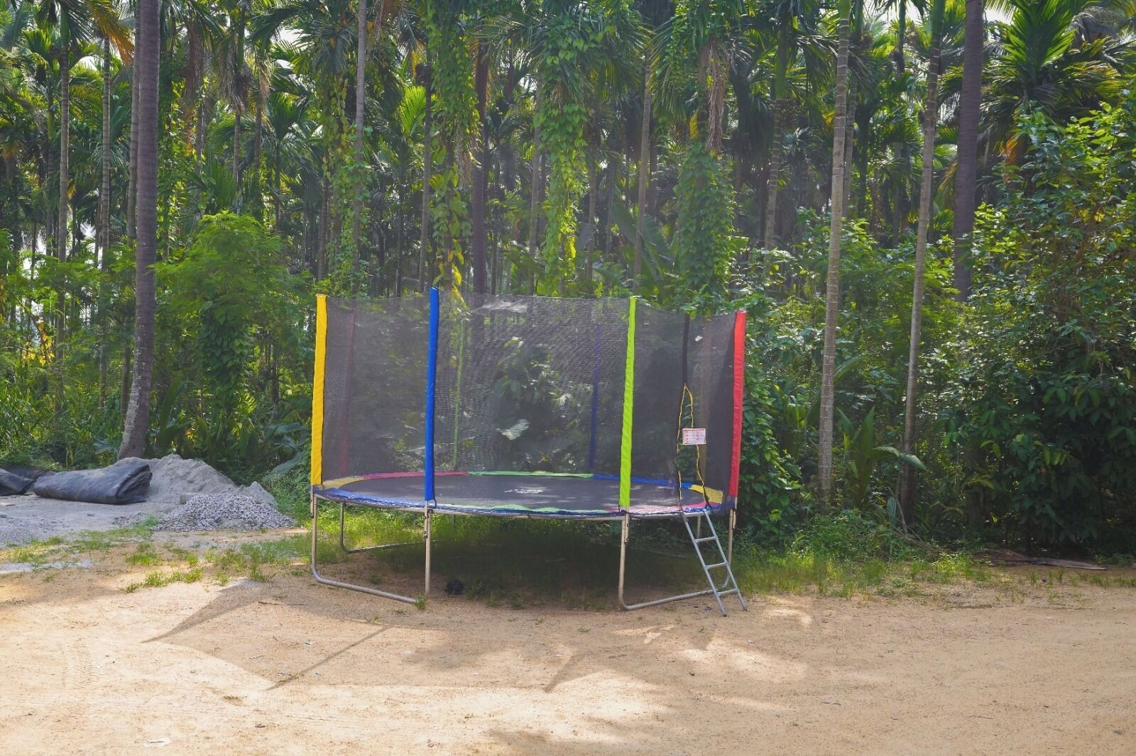 A trampoline set up outdoors with a safety net, surrounded by dense greenery and trees.