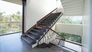 A modern staircase with a wooden handrail and black railings, leading to a balcony with a view of palm trees.
