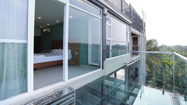 A modern hotel room with a glass balcony, a bed, and a view of the surrounding landscape.