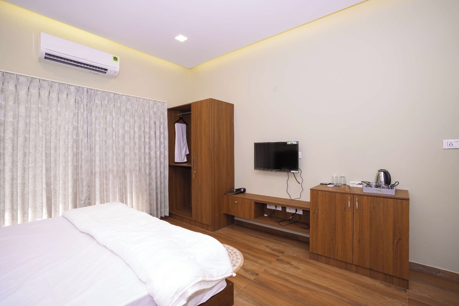A hotel room with a bed, a TV, a wooden wardrobe, and an air conditioning unit.