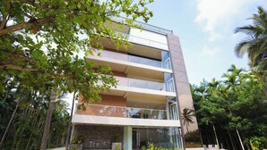 A multi-story building with balconies, surrounded by lush greenery and palm trees.