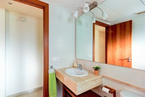 A modern bathroom with a wooden vanity, a white sink, a mirror, and a small potted plant. - Apartment in Roses With Beachfront Views (Roses)