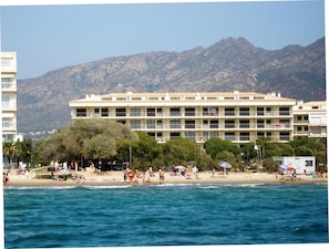 A beachfront hotel with multiple floors, a sandy beach in front, and mountains in the background. - Apartment in Roses With Beachfront Views (Roses)