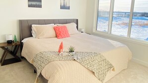 Un dormitorio con una cama grande, una mesita de noche, una ventana con vista a un paisaje nevado y dos cuadros colgados en la pared.