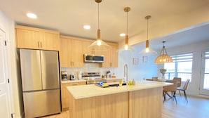 Una cocina moderna con armarios de madera, electrodomésticos de acero inoxidable e iluminación colgante.