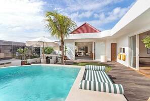 Una casa moderna con piscina, terraza de madera y tejado de tejas rojas.
