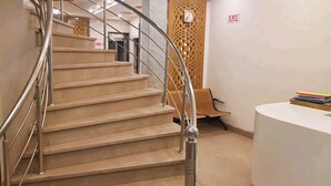 A modern staircase with metal railings and beige steps, leading to a reception area with a desk and a chair. - Hotel Leo Continental  (New Delhi)