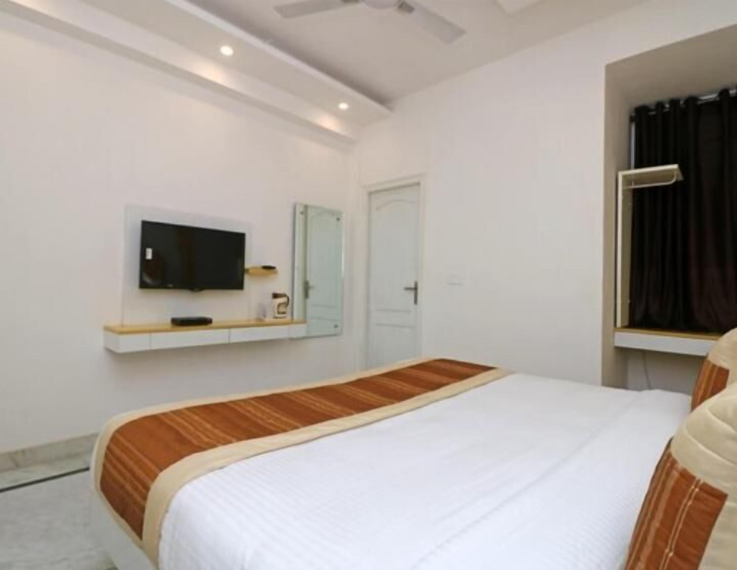 A bedroom with a bed, a TV mounted on the wall, a door, and a window with curtains.