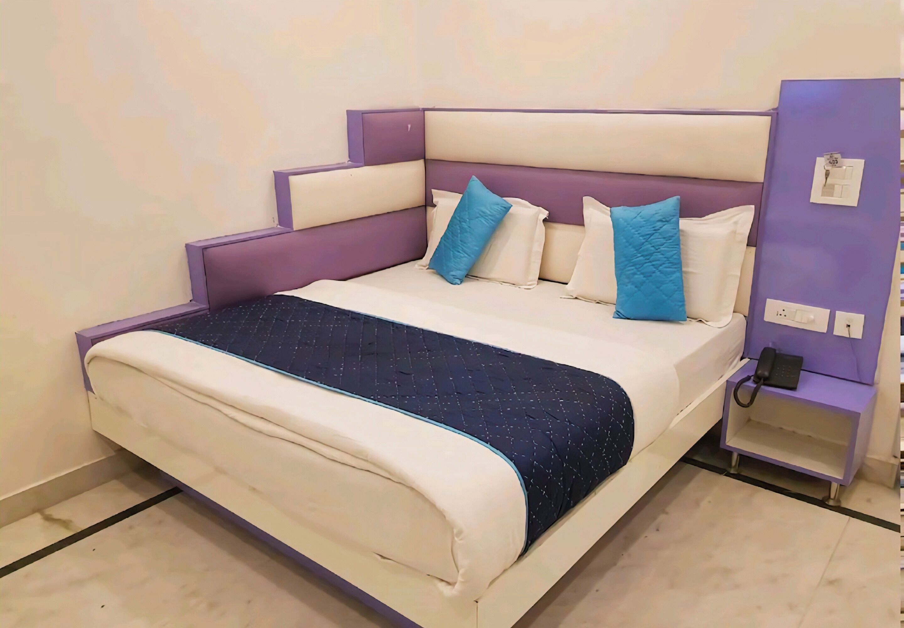 A bed with a headboard, pillows, and a bedside table with a phone.