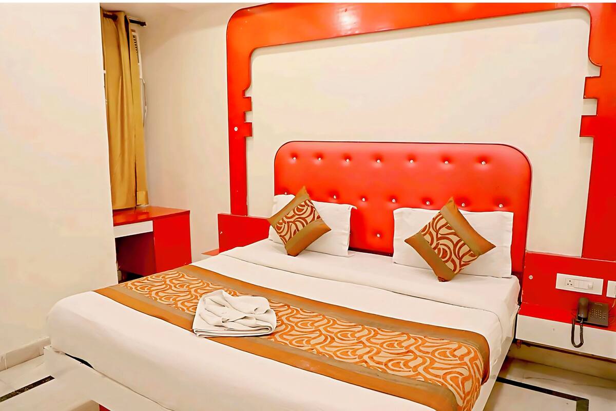 Quarto de hotel com cabeceira vermelha, roupa de cama branca e manta decorativa estampada.