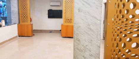 A reception area with a marble floor, wooden reception desk, and a wall-mounted TV.