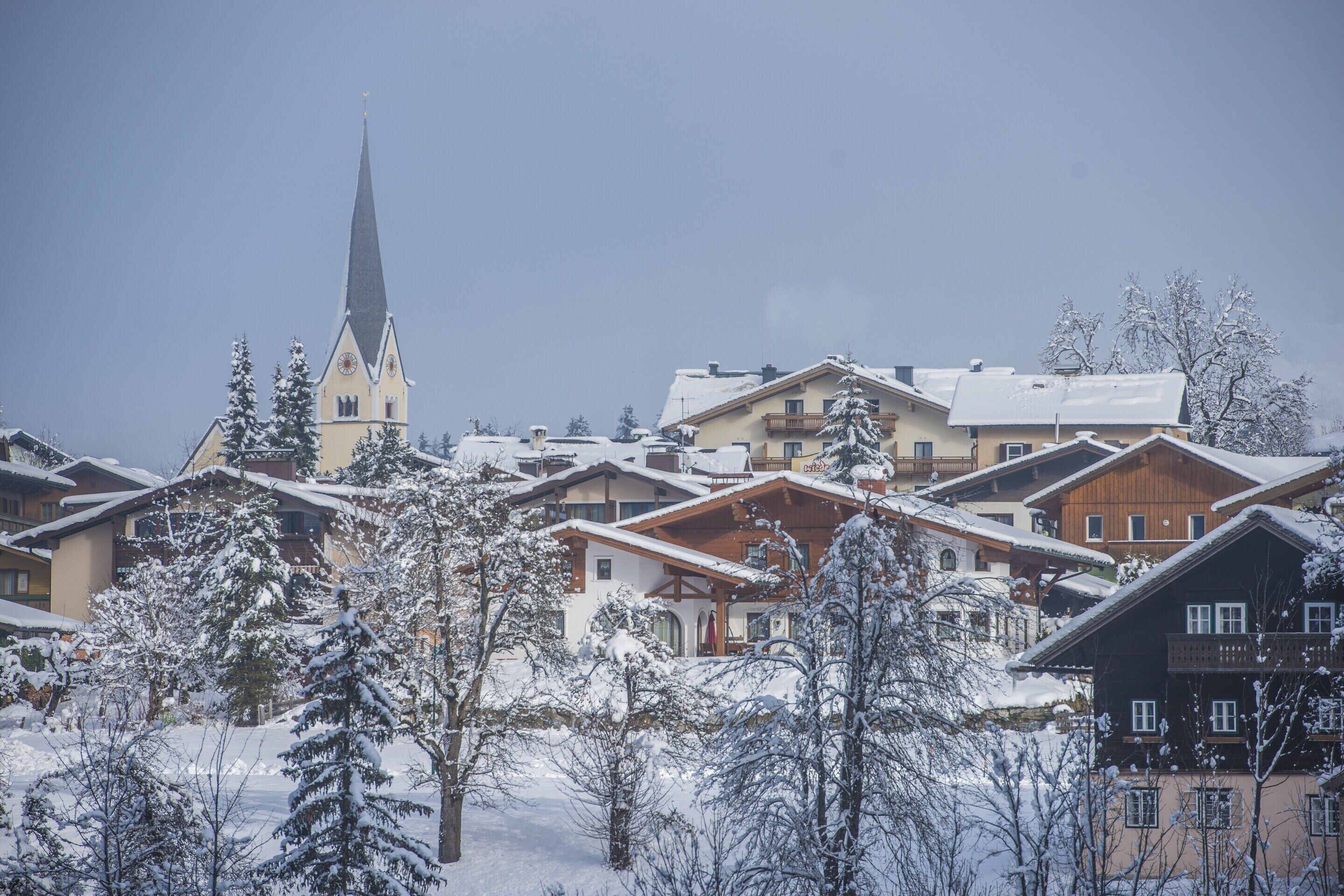 A snow-covered village with traditional wooden houses, a church with a tall steeple, and a clear sky.