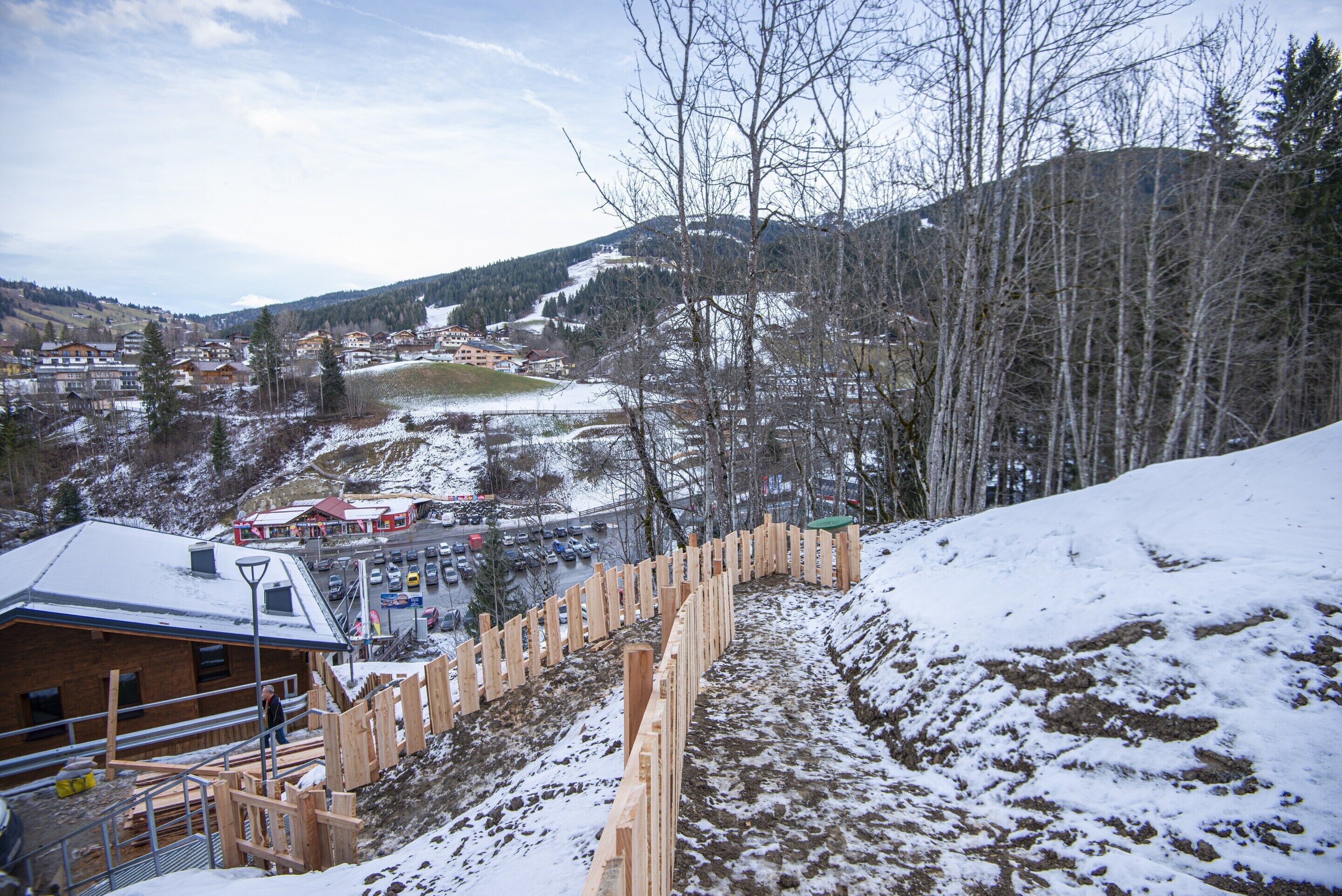 A snow-covered landscape with a wooden fence, buildings, and a distant view of a town.
