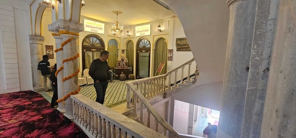 A grand staircase leading to a dormitory hall with ornate railings and a chandelier.