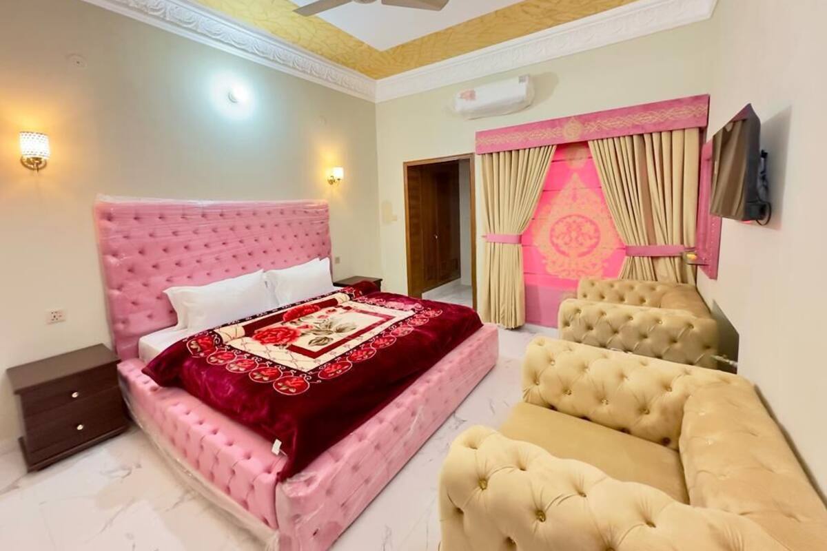 Un dormitorio con una cama tapizada rosa, un sofá beige y un ventilador de techo.