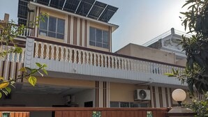 Een gebouw met twee verdiepingen, een balkon, zonnepanelen op het dak en een houten omheining.