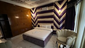 Een hotelkamer met een groot bed, een slaapbank, een kleine tafel met lamp en een plafondventilator.