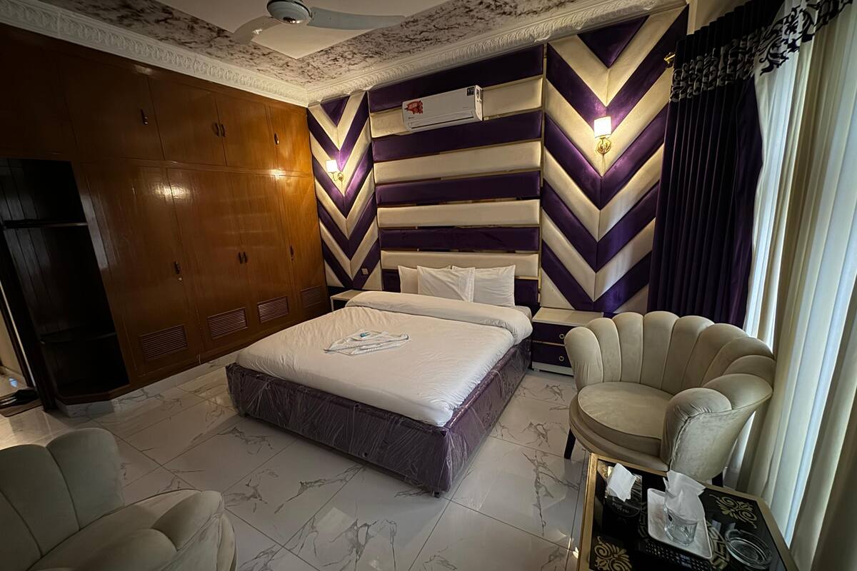 Habitación de hotel con una cama grande, un sofá, una mesita con lámpara y un ventilador de techo.