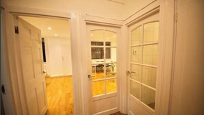 Un pasillo con puertas blancas que dan a una habitación con piso de madera y vista a un comedor.