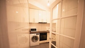 Una cocina compacta con armarios blancos, lavadora y microondas.