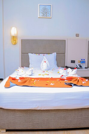 Une chambre d’hôtel avec un lit bien fait, une lampe de chevet, un tableau encadré au mur et une table de chevet avec un téléphone et des bouteilles d’eau.
