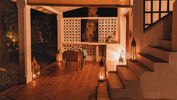 A covered outdoor dining area with a table set for two, a staircase, and decorative lanterns. - Beach front Mawimbi Studio in stunning garden (Coast)