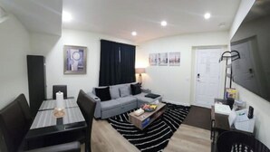 A compact living space with a dining table, sofa, and a TV mounted on the wall. - Charming Oasis Tranquil Suite 8 min Airport, AC (Calgary)