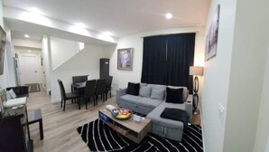 A modern living room with a grey sofa, a coffee table with snacks, a black and white striped rug, and a staircase leading to another room. - Charming Oasis Tranquil Suite 8 min Airport, AC (Calgary)