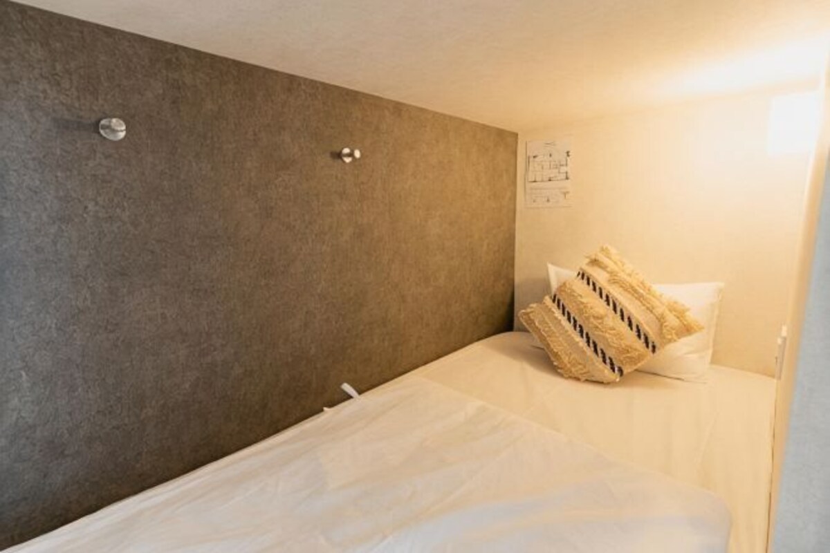 A hotel room with a bed, a headboard, a wall-mounted light, and a wall clock.