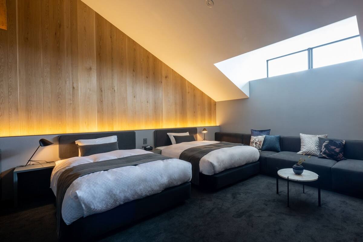 Ein modernes Hotelzimmer mit zwei Betten, einer Couch, einem kleinen Tisch und einem Oberlicht.
