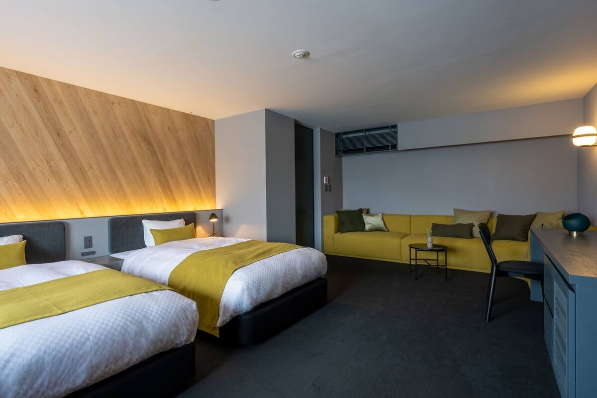 Ein Hotelzimmer mit zwei Betten, einem Sofa, einem Schreibtisch und einer Lampe.