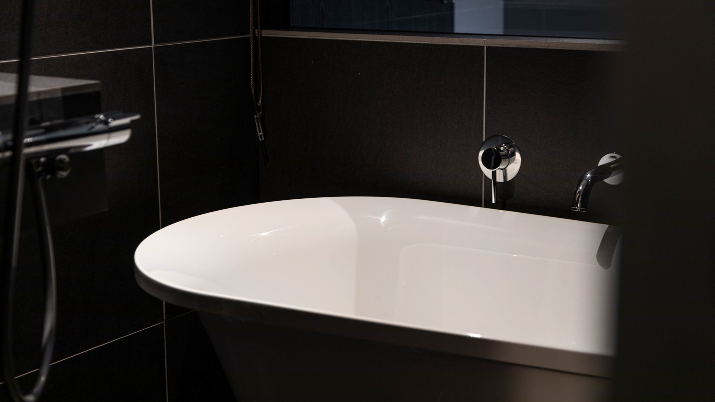 Ein modernes Badezimmer mit freistehender Badewanne, einer Handbrause und einem am Wand montierten Wasserhahn.