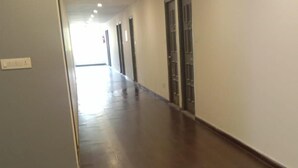 A long, narrow hallway with wooden flooring and white walls. - Hotel Neelkanth Inn (Ahmedabad)