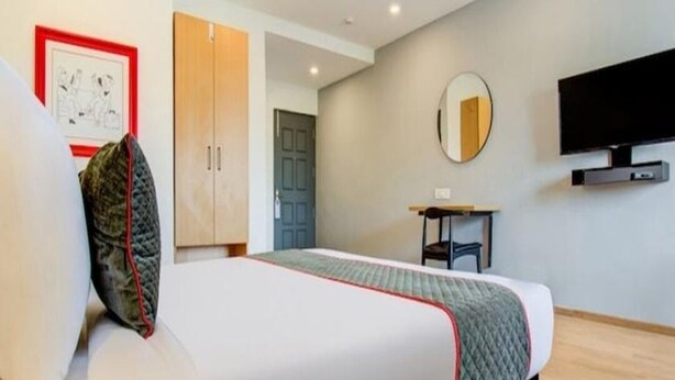 A modern hotel room with a bed, a desk, a mirror, and a TV. - Hotel Neelkanth Inn (Ahmedabad)