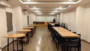 A conference room with multiple tables and chairs, wooden flooring, and recessed ceiling lighting. - Hotel Neelkanth Inn (Ahmedabad)