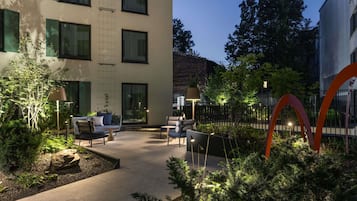 A modern outdoor seating area with tables and chairs, surrounded by greenery and a decorative metal structure.