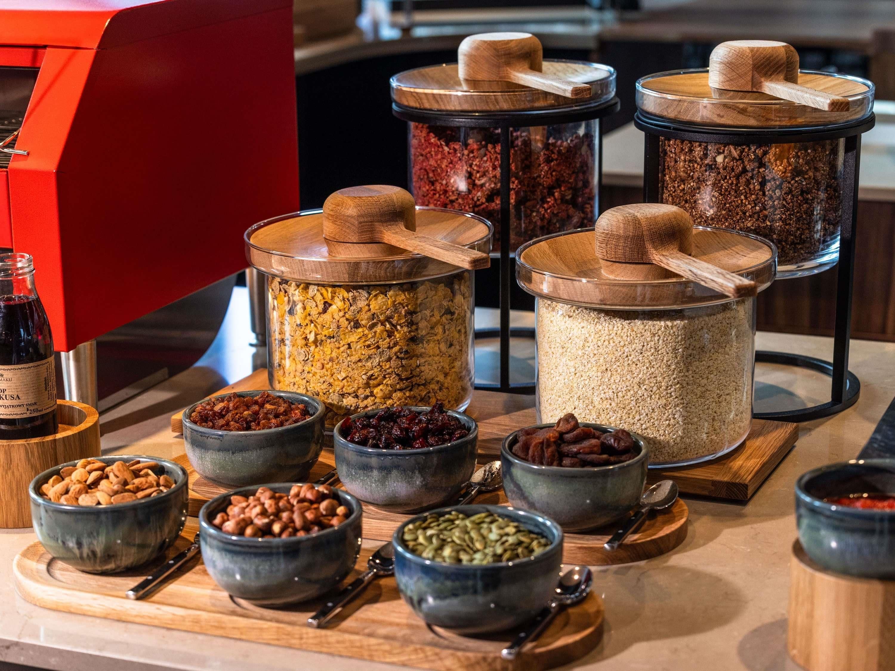 A variety of food items in containers, including grains, nuts, and dried fruits, arranged on a wooden board.