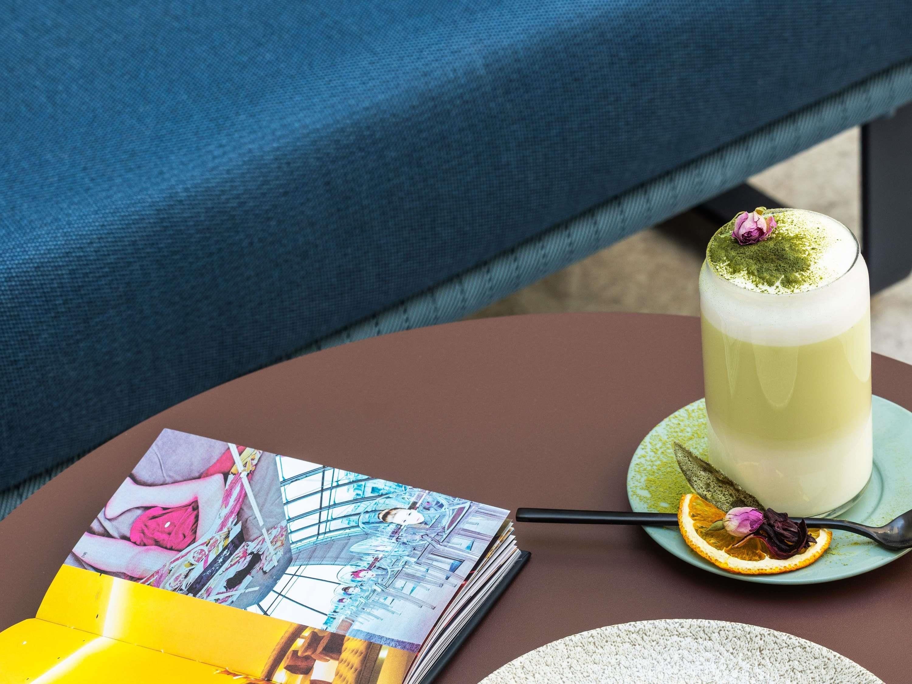 A table with a drink, a magazine, and a plate with a slice of orange.