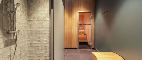 Un baño moderno con ducha, una zona de sauna de madera y un banco de madera.