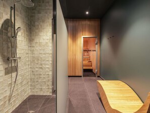 Un baño moderno con ducha, una zona de sauna de madera y un banco de madera.