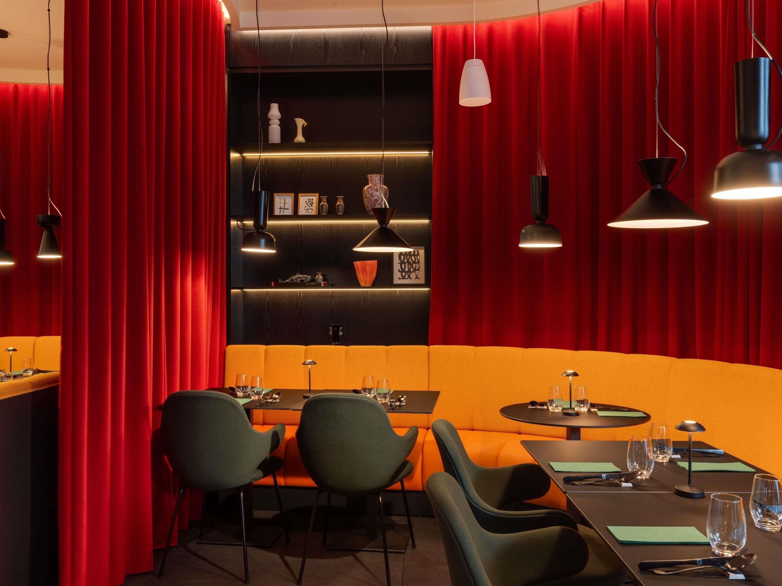 A restaurant with red curtains, a black wall with shelves, and orange seating.