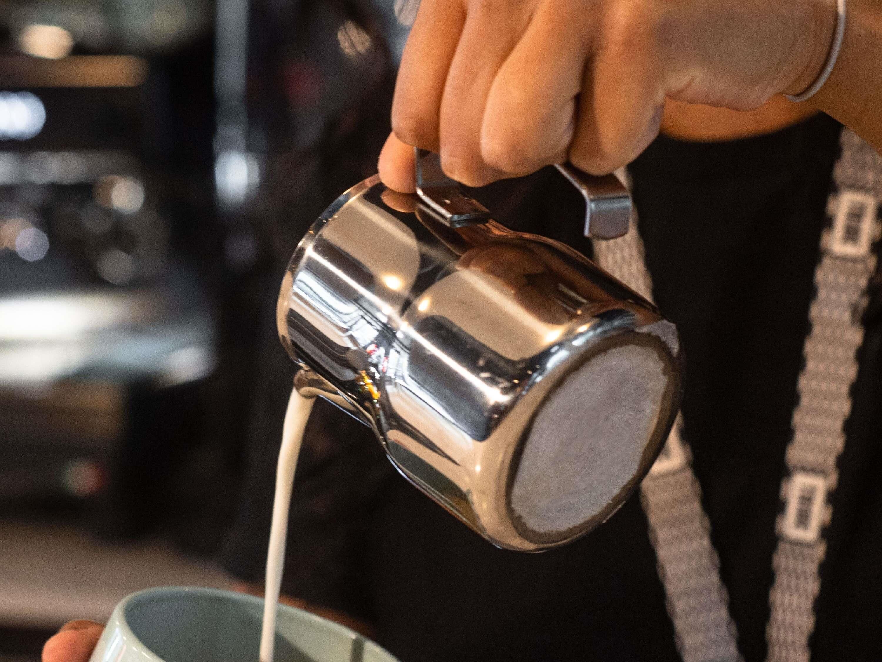 A person pouring a liquid from a metallic pitcher into a cup.