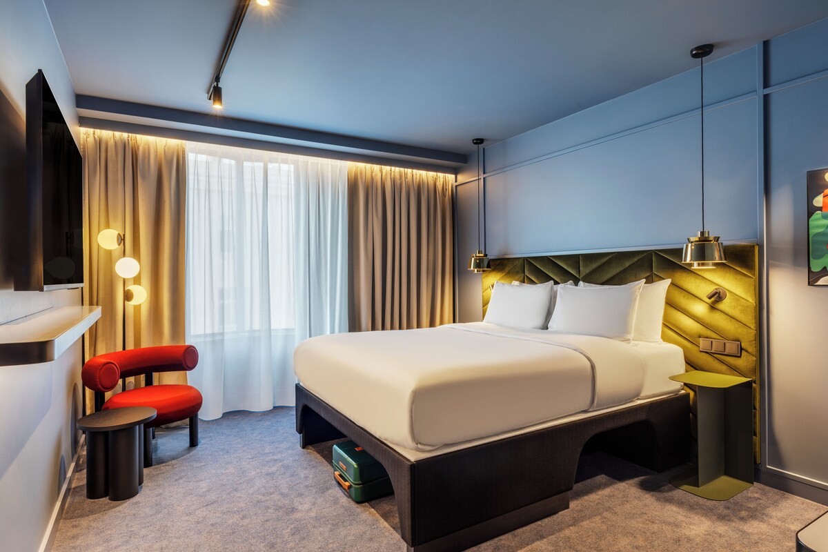 Ett modernt hotellrum med en stor säng, ett skrivbord, en stol och ett nattduksbord.