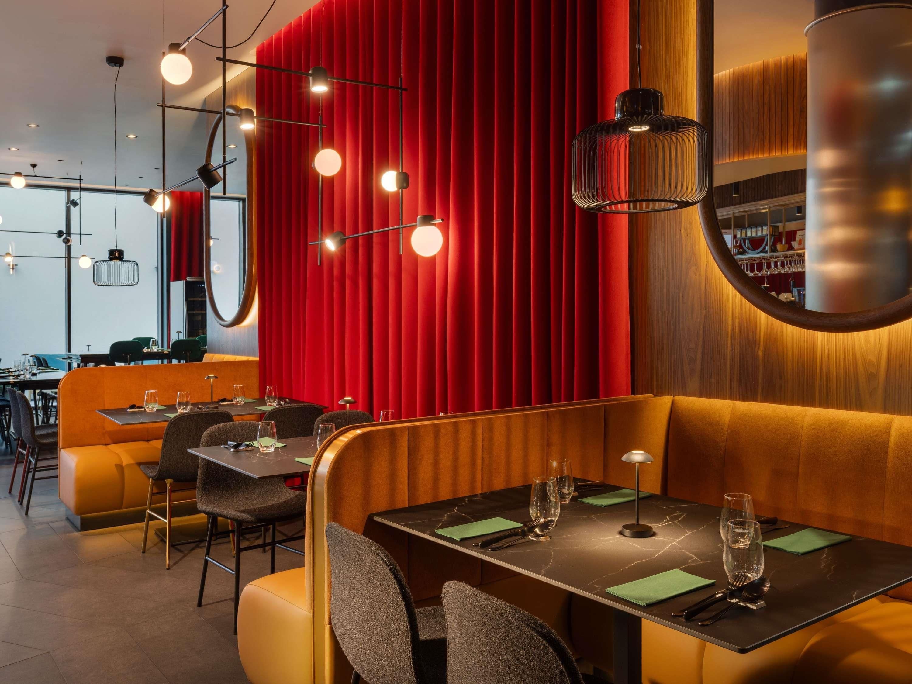 Un restaurant avec des banquettes, des tables et un rideau rouge en arrière-plan.