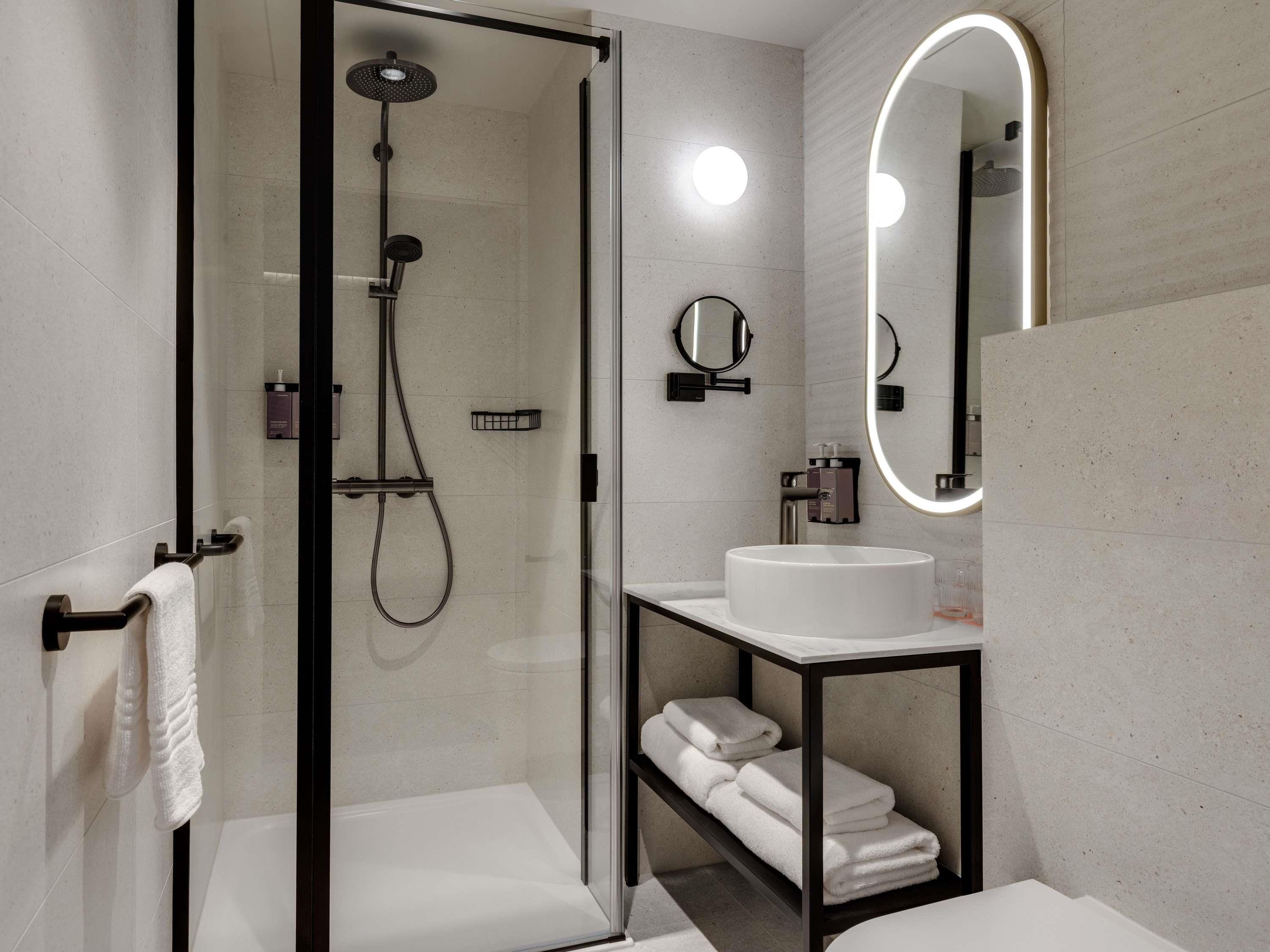 A modern bathroom with a glass-enclosed shower, a white sink, a mirror, and a towel rack.