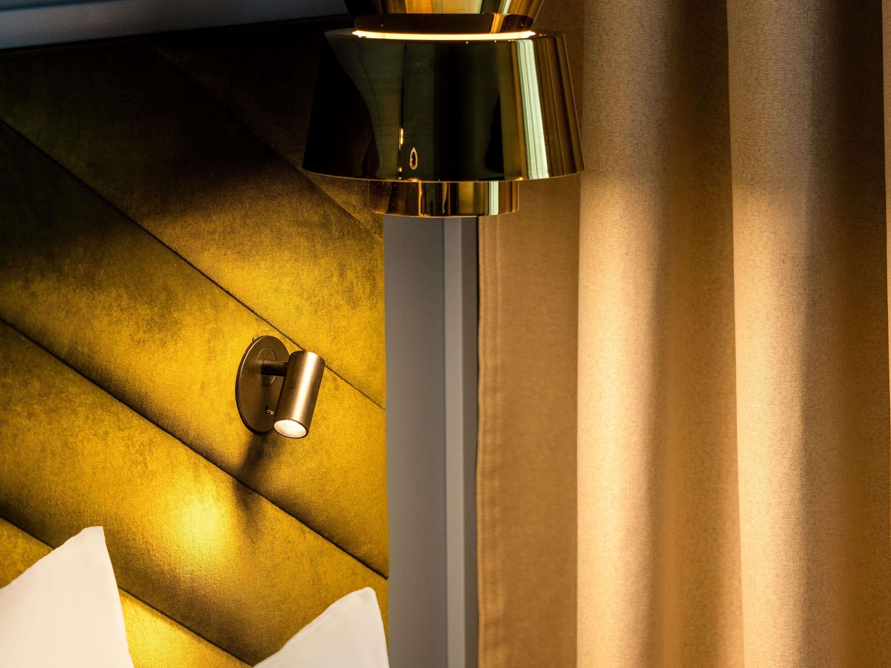 Une lampe moderne dotée d’un abat-jour cylindrique et d’un pied métallique, placée sur un mur à texture.