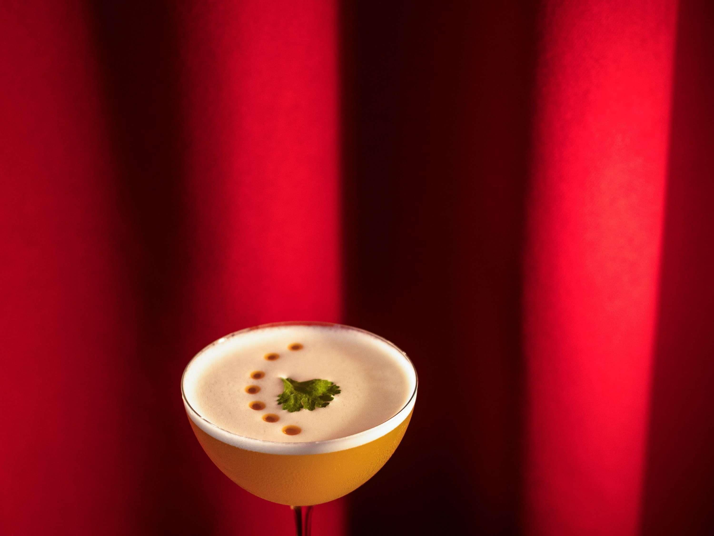 A cocktail in a martini glass with a garnish, set against a red background.